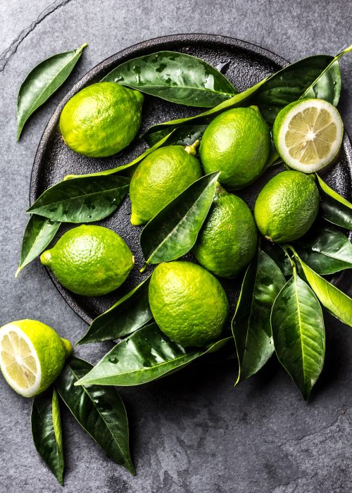 Green lemon Lime with fresh leaves on black plate, slate background